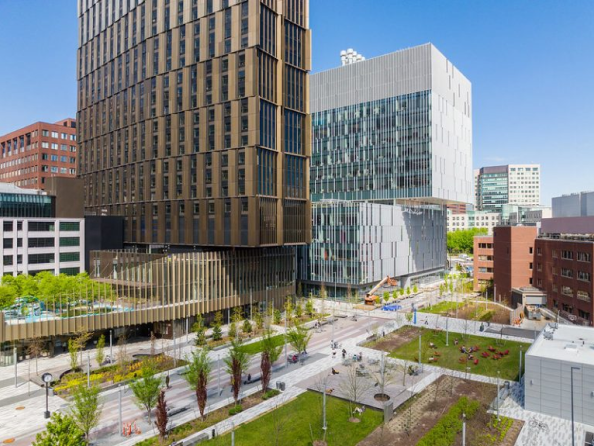 Aerial view of a graduate residence tower in Kendall Square rising above the MIT Welcome Center and surrounding landscaped green space.
