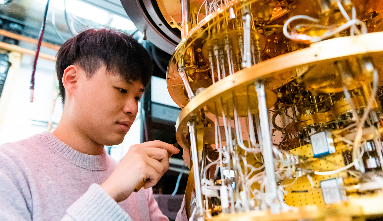 Postdoctoral researcher Ilan Rosen standing beside a dilution refrigerator used to cool qubits to near absolute zero.