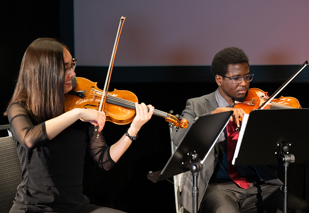 Two students play violins on stage at MIT's Infinite Possibilities event.