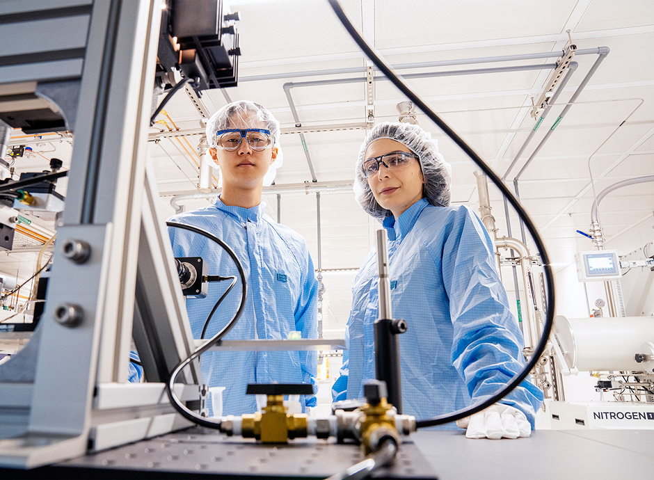 Associate Professor Farnaz Niroui and graduate student Spencer Zhu in cleanroom suits and protective headgear inside a MIT.nano cleanroom.