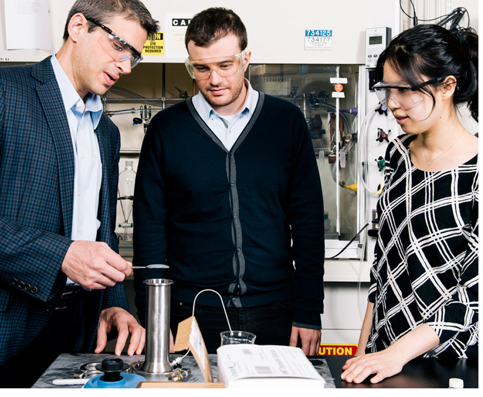 Jeffrey Grossman and two students, all in protective goggles, work in a materials science lab.
